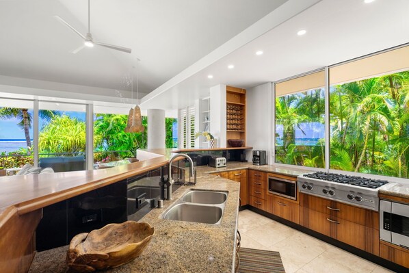 A modern kitchen with a large island, built-in appliances, and a view of lush greenery.