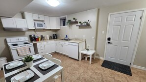 Une cuisine compacte avec des meubles blancs, un four à micro-ondes, une cuisinière et un petit coin repas avec une table mise pour deux personnes.