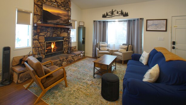 A living room with a stone fireplace, a blue sofa, a wooden chair, and a coffee table.
