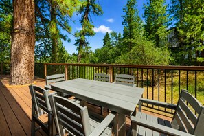 Eine Terrasse im Freien mit Tisch und Stühlen, umgeben von Bäumen und einem wolkenlosen Himmel.