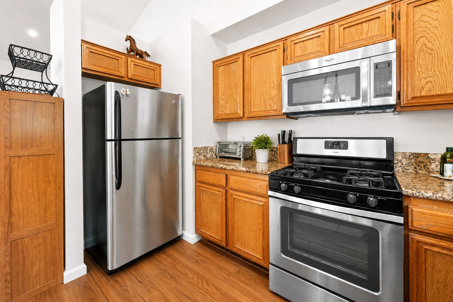 A kitchen with wooden cabinets, a stainless steel refrigerator, a microwave, a stove, and a toaster.