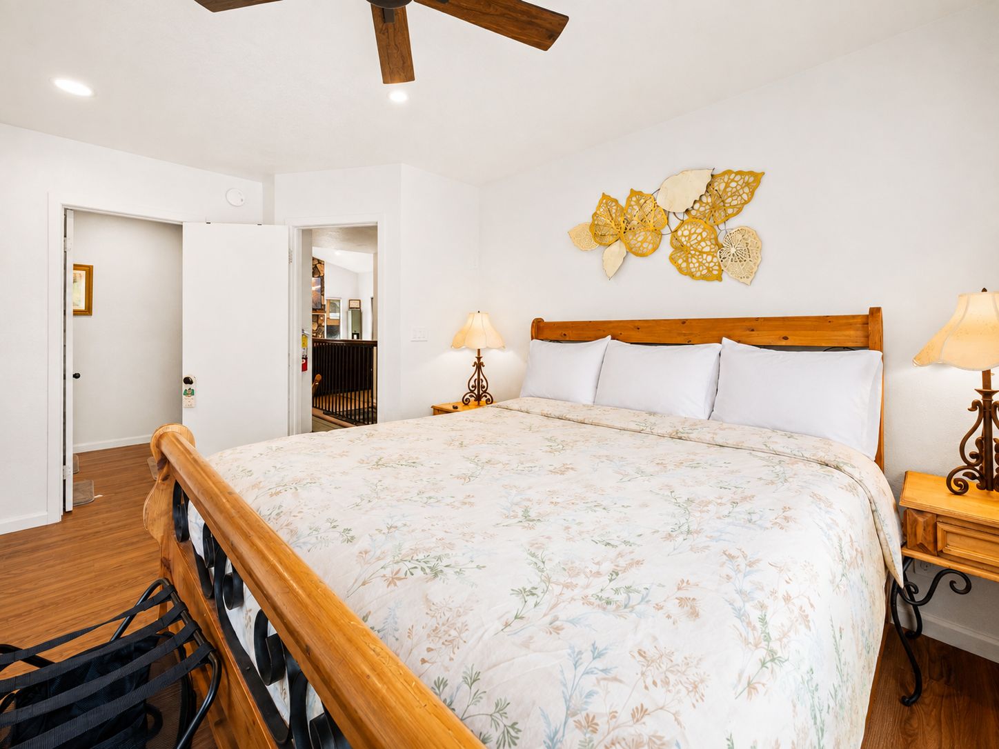 A bedroom with a wooden bed, a ceiling fan, a wall-mounted lamp, and a door leading to another room.