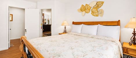 A bedroom with a wooden bed, a ceiling fan, a wall-mounted lamp, and a door leading to another room.