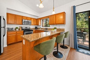 Een moderne keuken met houten kastjes, granieten aanrechtbladen en een centraal eiland met barkrukken.