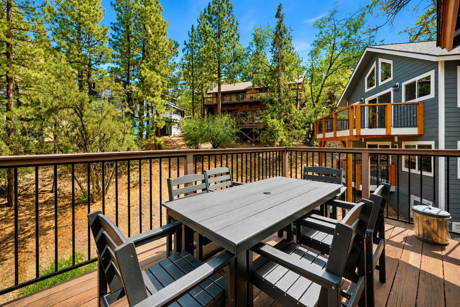Une terrasse dotée d’une table et de chaises, entourée d’une rambarde en bois, et offrant une vue sur une zone boisée.