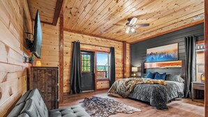 A log cabin bedroom with a bed, a sofa, a ceiling fan, and a painting on the wall. - Amazing BRAND NEW 8bdrm Cabin-Pool-Arcades-Gazebo (Sevierville)