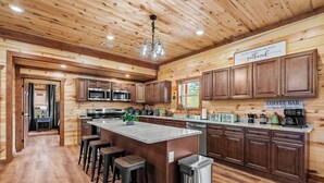 A spacious kitchen with wooden cabinets, a central island with stools, a coffee bar, and a sign that reads "The Best Memories Are Made at Gathered." - Amazing BRAND NEW 8bdrm Cabin-Pool-Arcades-Gazebo (Sevierville)
