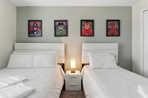 A hotel room with two beds, white bedding, and framed posters of Captain America, Hulk, Iron Man, and Spider-Man on the wall.