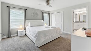 Ein Schlafzimmer mit Bett, Nachttischen, Deckenventilator und Blick ins Badezimmer.