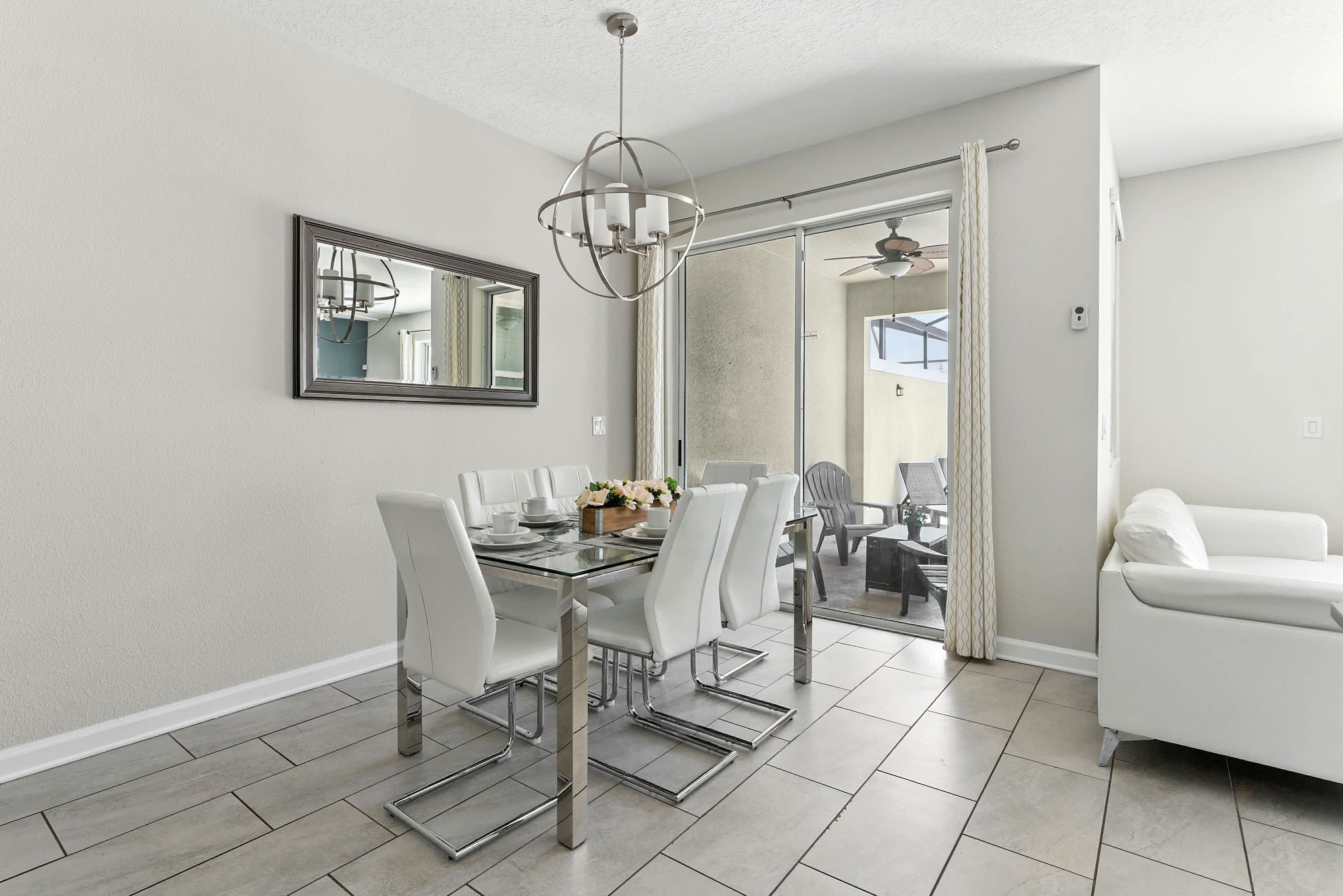 A dining area with a glass table, white chairs, and a modern chandelier.