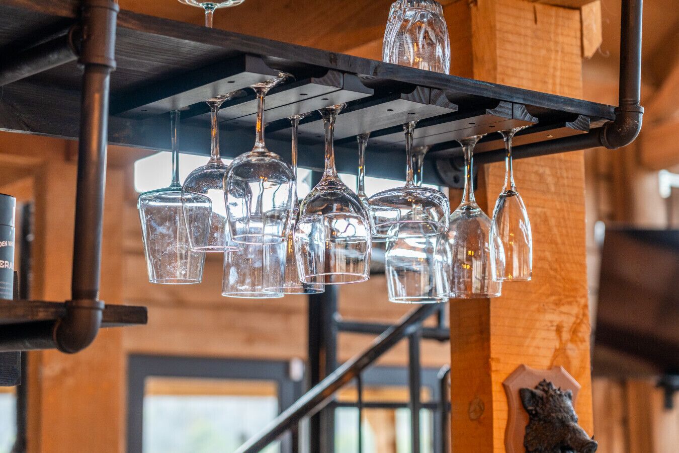 Une série de verres à vin transparents suspendus à un présentoir métallique dans un intérieur rustique en bois.