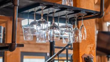 Une série de verres à vin transparents suspendus à un présentoir métallique dans un intérieur rustique en bois.