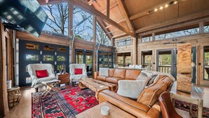 A spacious cabin interior with a large wooden ceiling, a cozy seating area with leather sofas and chairs, and a vibrant red rug.