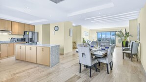Una cocina moderna con una isla central, comedor con mesa y sillas, y un amplio ventanal con vistas a la ciudad.