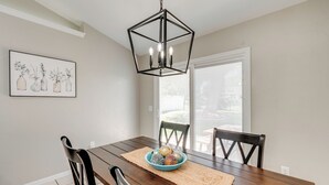 Comedor con mesa de madera, sillas negras, un tazón azul con adornos y una lámpara colgante de diseño geométrico.