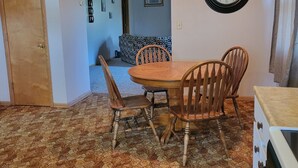 A dining area with a wooden table and chairs, a clock on the wall, and a patterned floor. - Peaceful Nostalgic Farmhouse (Plankinton)