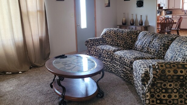 A living room with a patterned sofa, a glass-top coffee table, a ceiling fan, and a door with a window. - Peaceful Nostalgic Farmhouse (Plankinton)