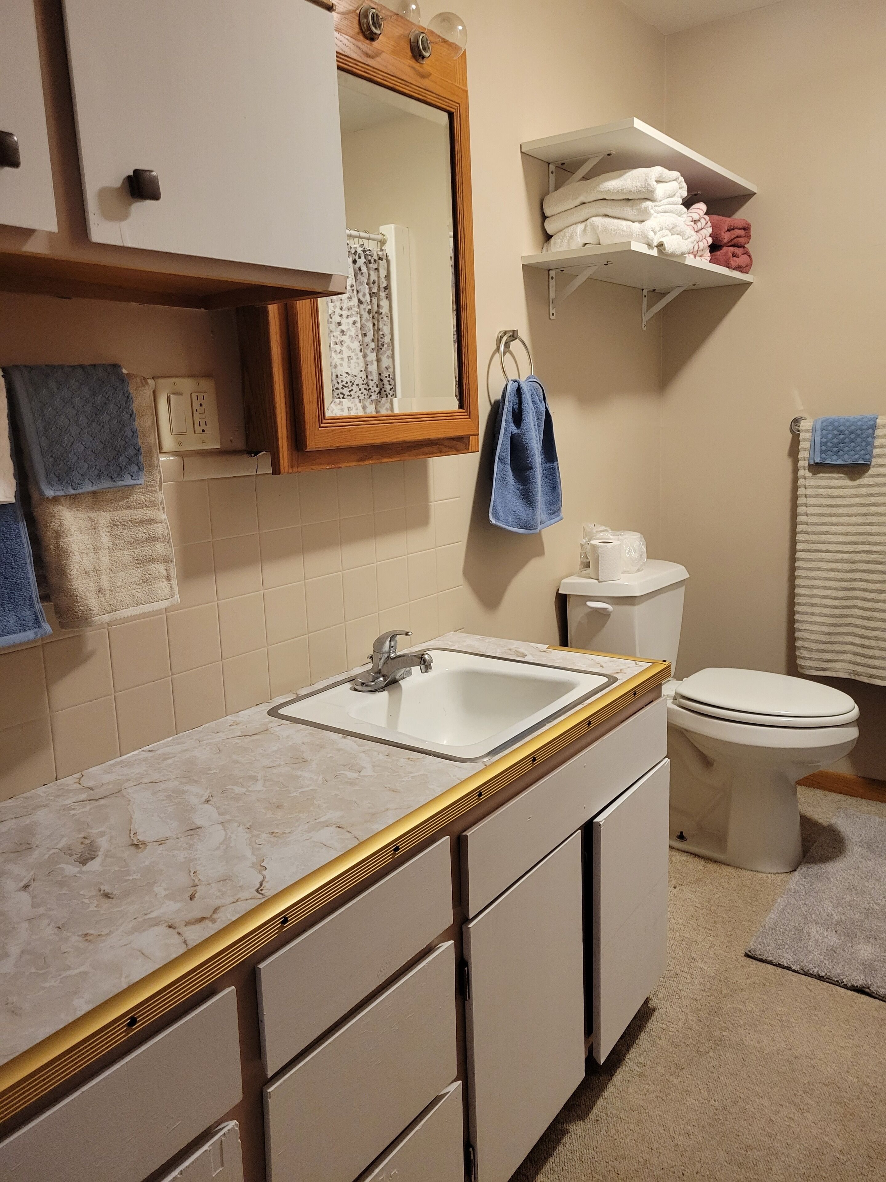 A bathroom with a sink, toilet, and shelves with towels.