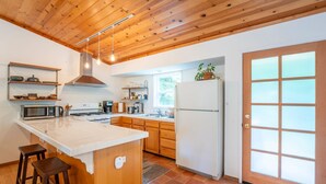 A kitchen with wooden cabinets, a white island, a microwave, a stove, and a refrigerator. - Coastal Redwood Bliss | Little River (Little River)