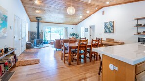 A spacious living area with a wooden ceiling, a stone fireplace, and a dining table with chairs. - Coastal Redwood Bliss | Little River (Little River)