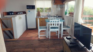 Una cocina compacta con microondas, refrigerador, pileta y cocina. Hay un pequeño comedor con una mesa y sillas. Un televisor está sobre un atril de madera.