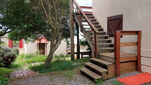 Una escalera de madera que lleva a un edificio con zócalo rojo y una puerta con contraventanas de madera.