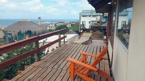 Een houten terras met een leuning, een bankje en uitzicht op zee en gebouwen.