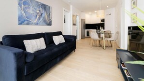 A modern living room with a dark blue sofa, a dining area with a glass table, and a kitchen in the background. - Aurora Stays by Charming III, Apartment for 4 with free parking (Madrid)