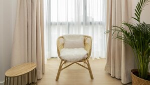Une pièce avec un fauteuil en osier, une petite table en bois et une plante en pot.