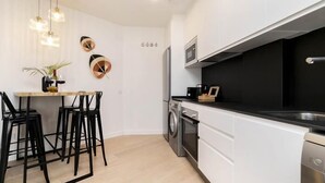 Une cuisine moderne avec des meubles blancs, un plan de travail noir et des appareils en acier inoxydable. On y trouve un coin repas avec des chaises noires et une table en bois.