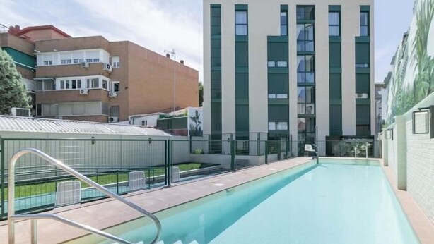 Una piscina con escalera de metal, rodeada de edificios modernos con grandes ventanales y tejados planos.