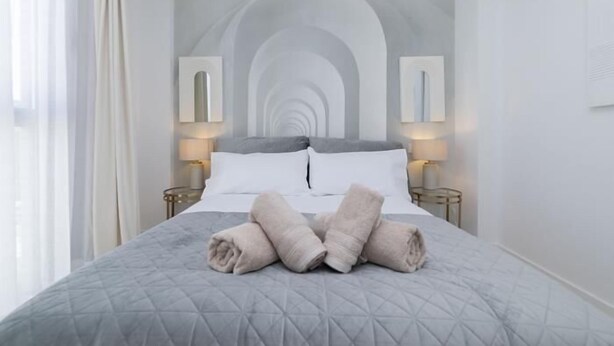 A neatly made bed with rolled towels, a quilted gray bedspread, and two bedside lamps.