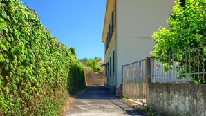 Une ruelle étroite, pavée, bordée d’une haute haie et d’un immeuble à la façade beige.