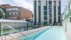 Ein Schwimmbecken mit einer Metallleiter, umgeben von modernen Gebäuden mit großen Fenstern und flachem Dach.