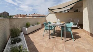 Eine Dachterrasse mit Tisch und Stühlen, einem integrierten Blumenkasten und einem ausrollbaren Sonnensegel.