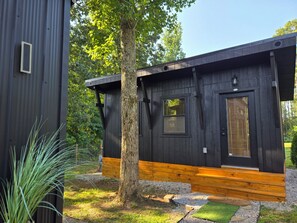 A modern cabin with a dark exterior, a wooden deck, and a small window.