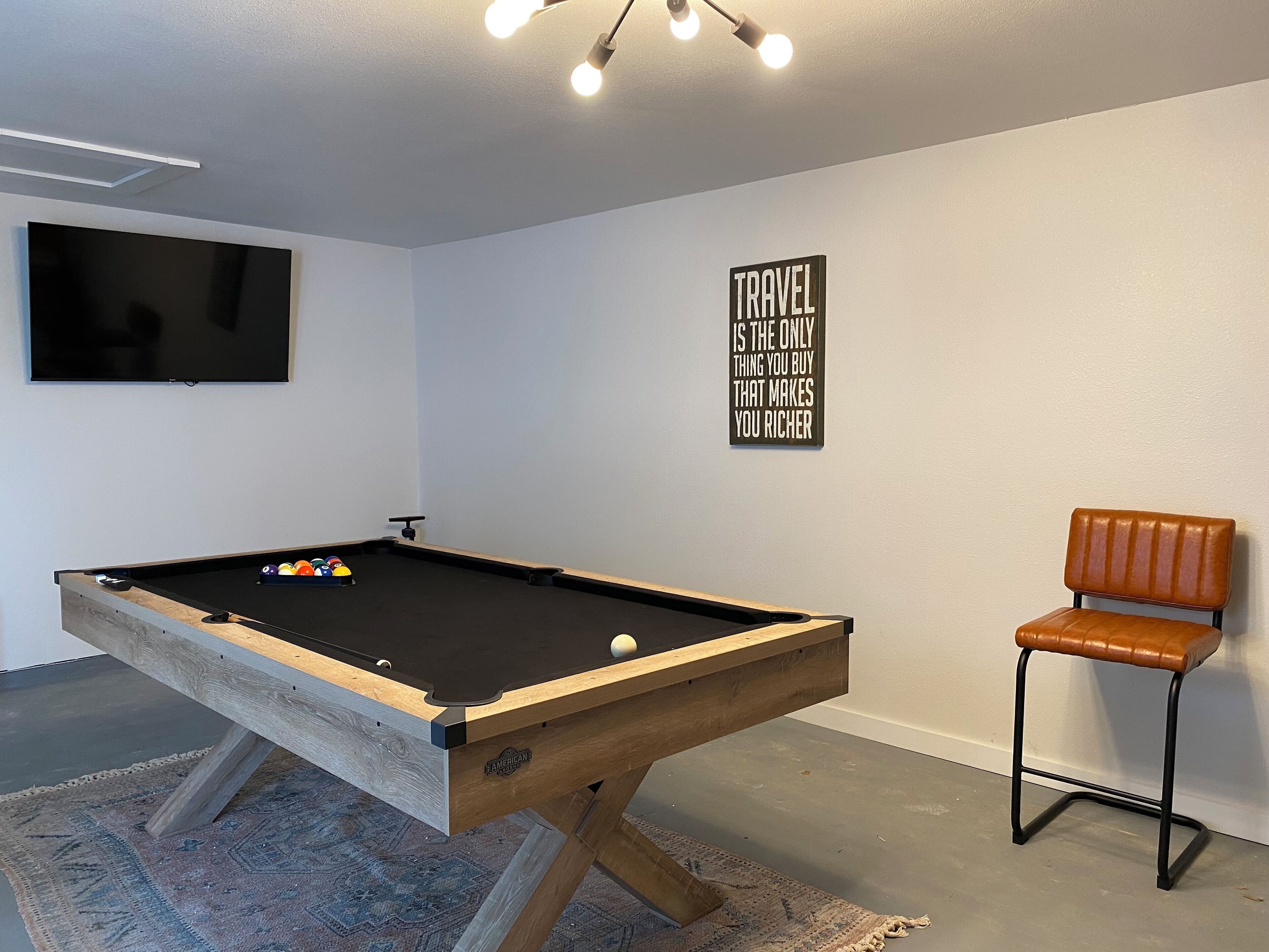 Una mesa de billar con un televisor montado, una frase motivacional en la pared y un sillón de cuero marrón.