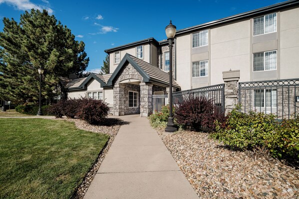 A building with a stone facade, a central entrance with a stone archway, and a paved pathway leading to the entrance. - Ville 7877 (Englewood)