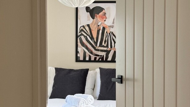 Una habitación de hotel con una cama, almohadas, una toalla enrollada y un cuadro en la pared.
