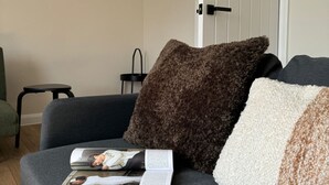 Un sofá gris con una revista y cojines en una habitación con una puerta y una mesita.