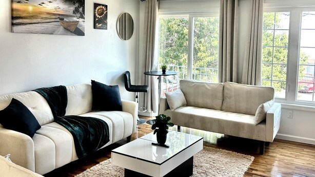 Una sala de estar moderna con dos sofás, una mesa de centro y un ventanal con cortinas.