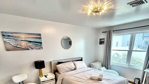 Un dormitorio moderno con una cama grande, mesitas de noche, una silla, una alfombra y un ventanal con vistas.