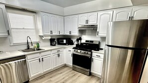 Una cocina moderna con armarios blancos, un refrigerador de acero inoxidable, un microondas y una estufa.