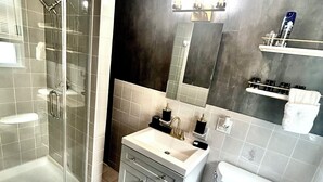 Un baño moderno con ducha envuelta en vidrio, un lavamanos blanco y un inodoro.