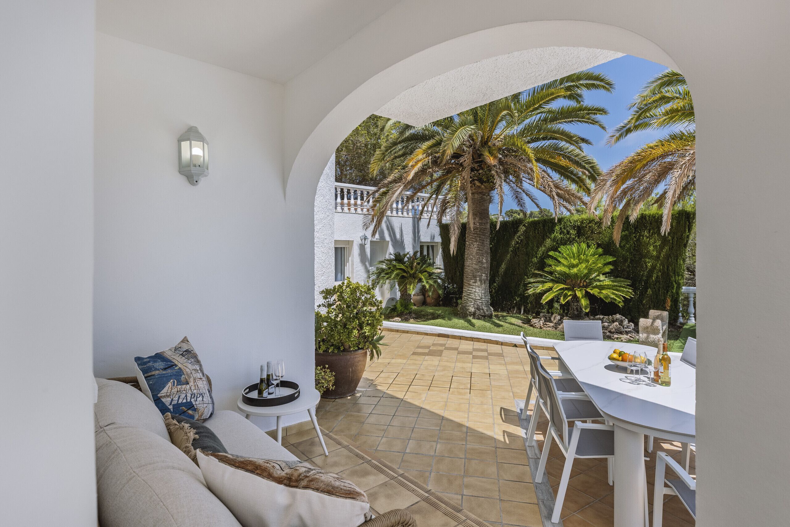 Une terrasse avec une table et des chaises blanches, un canapé avec des coussins et une plante en pot.