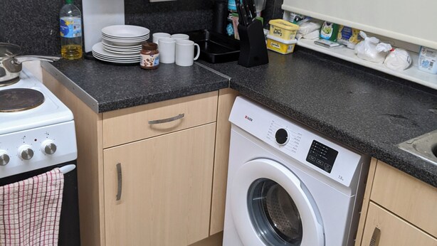 A compact kitchen with a stove, a washing machine, and various kitchen items on the countertop. - Birch Cabin Retreat in Girvan (Girvan)