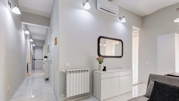 A modern, well-lit hallway with a radiator, a white cabinet, and a sofa with a cushion.