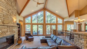 A spacious living area with a stone fireplace, leather sofas, and large windows offering a view of the outdoors. - River Bend on Fall River - Riverfront property! (Estes Park)