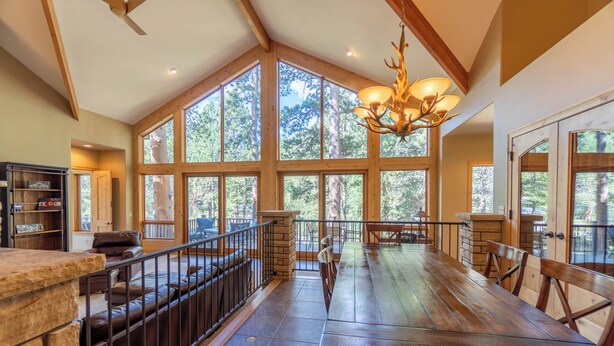 A spacious room with large windows, a wooden dining table, and a stone fireplace. - River Bend on Fall River - Riverfront property! (Estes Park)
