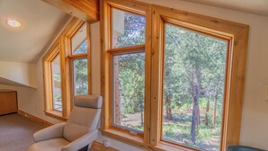 A room with large windows, a reclining chair, and a view of a forest. - River Bend on Fall River - Riverfront property! (Estes Park)